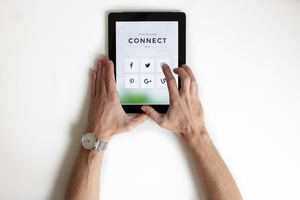 Imagem destacada do post da Dotin Digital referente a empresa marcar presença nas redes sociais, onde uma pessoa segura um tablet com vários ícones de redes sociais.