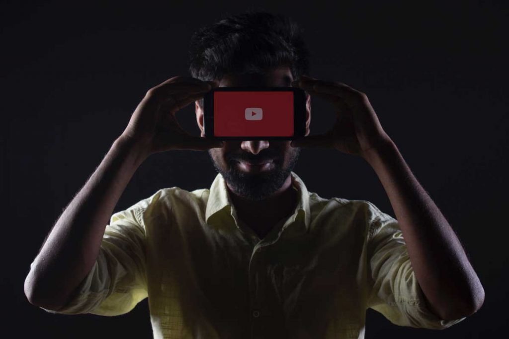 Homem segurando um smartphone com a página de splash do youtube. Produção de visual é uma tendência de marketing digital.