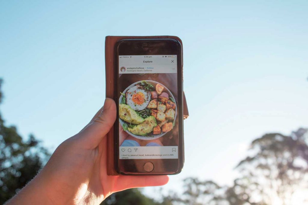 Pessoa segurando um smartphone com uma postagem do instagram de um prato de comida.