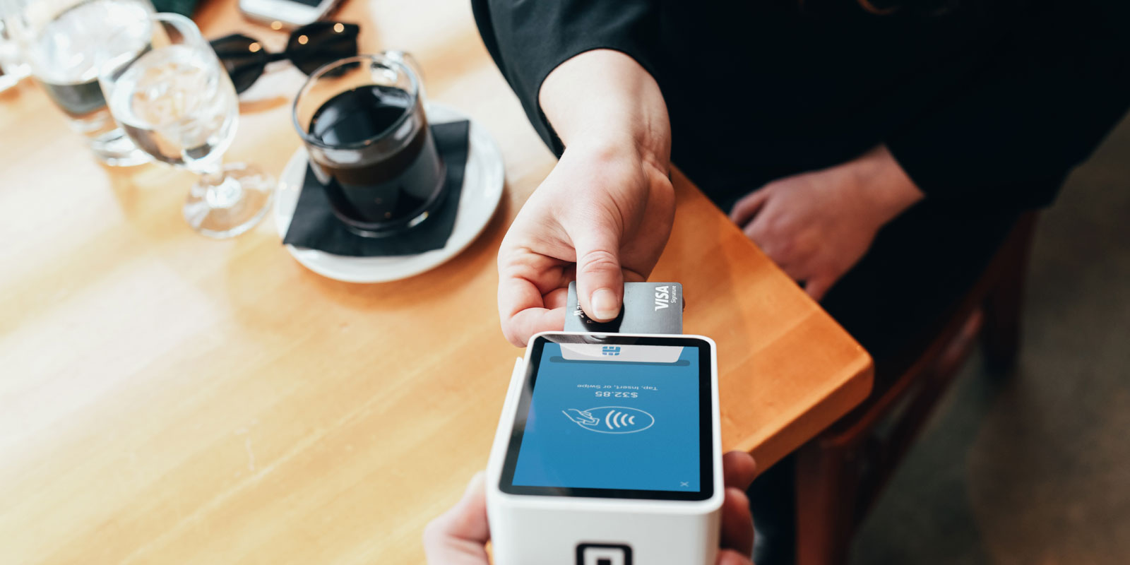 Imagem de uma pessoa pagando seu café em uma maquina de cartão de crédito.
