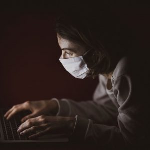 pessoa acessando o computador utilizando máscara buscando inovação durante a pandemia de coronavírus